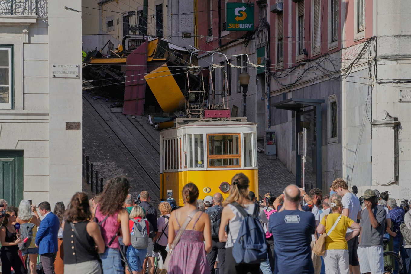 Nyfikna tittar upp mot olycksplatsen i backen i centrala Lissabon på torsdagen. Foto: Armando Franca/AP/TT