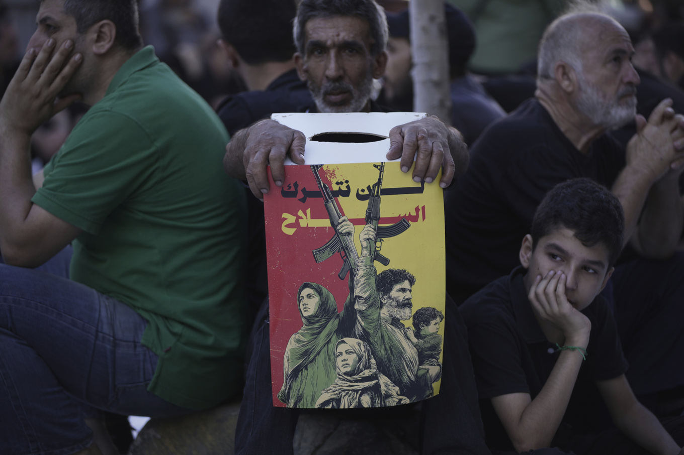 En Hizbollahsupporter håller i en poster med texten "Vi kommer inte att överge våra vapen" i en förort till Beirut, Libanon i juli 2025. Foto: Hassan Ammar/AP/TT
