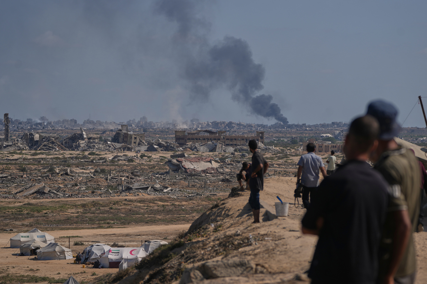Palestiniser som tvingats på flykt av Israels utökade militära offensiv i norra Gaza blickar mot svarta rökpelare som stiger mot himlen efter attacker i Gaza stad under torsdagen. Foto: Abdel Kareem Hana/AP/TT