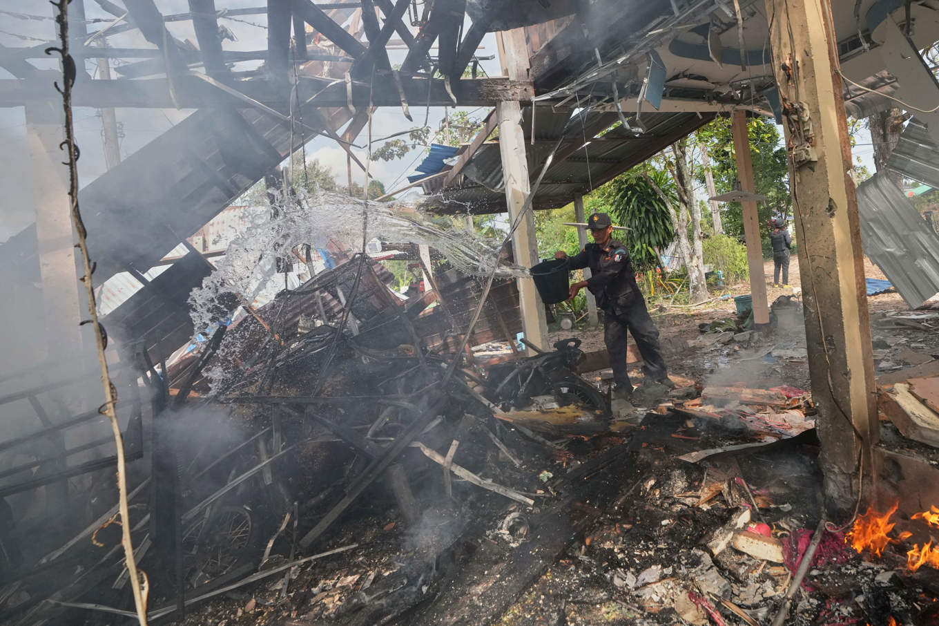 En frivillig säkerhetsvakt försöker släcka en brand i ett hus i provinsen Sisaket i Thailand på söndagen. Både Thailand och Kambodja anklagar varandra för nya attacker. Foto: Sakchai Lalit/AP/TT