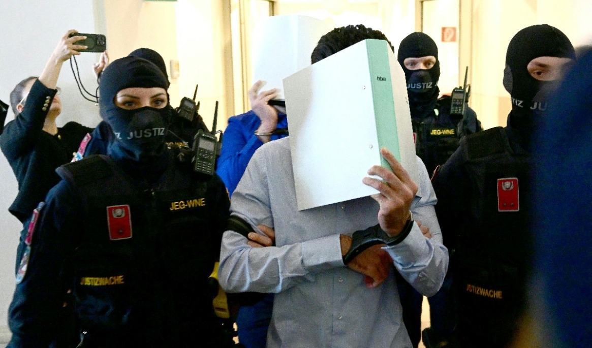 Två åtalade i handbojor eskorteras in i rättssalen av vakter när rättegången inleds vid domstolen i Wiener Neustadt i Österrike den 28 april. Foto: Roland Schlager/APA/AFP via Getty Images