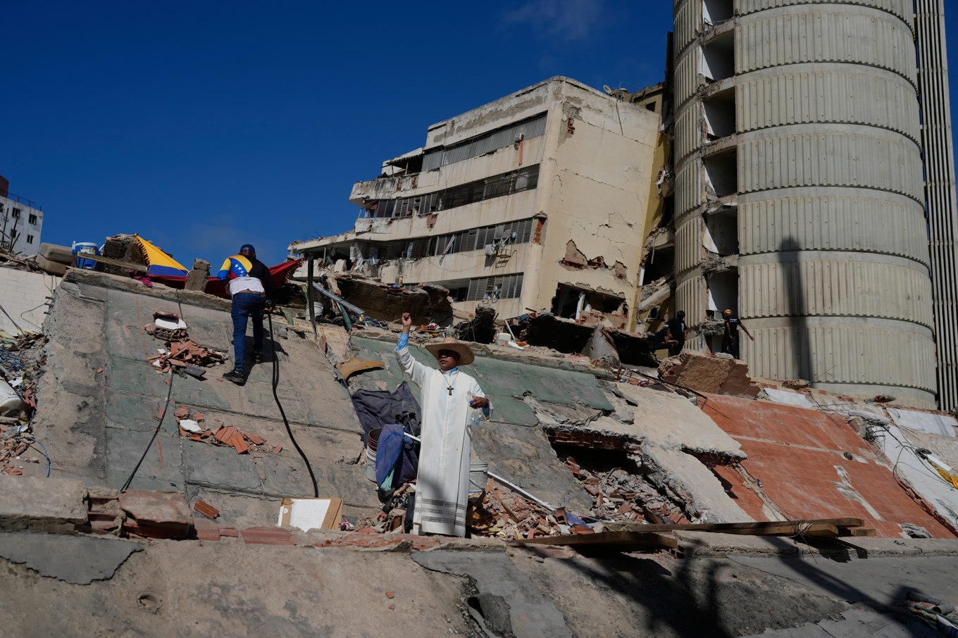 En katolsk präst står bland rasmassorna från bostadshus. Bild från i fredags. Foto: Ariana Cubillos/AP/TT