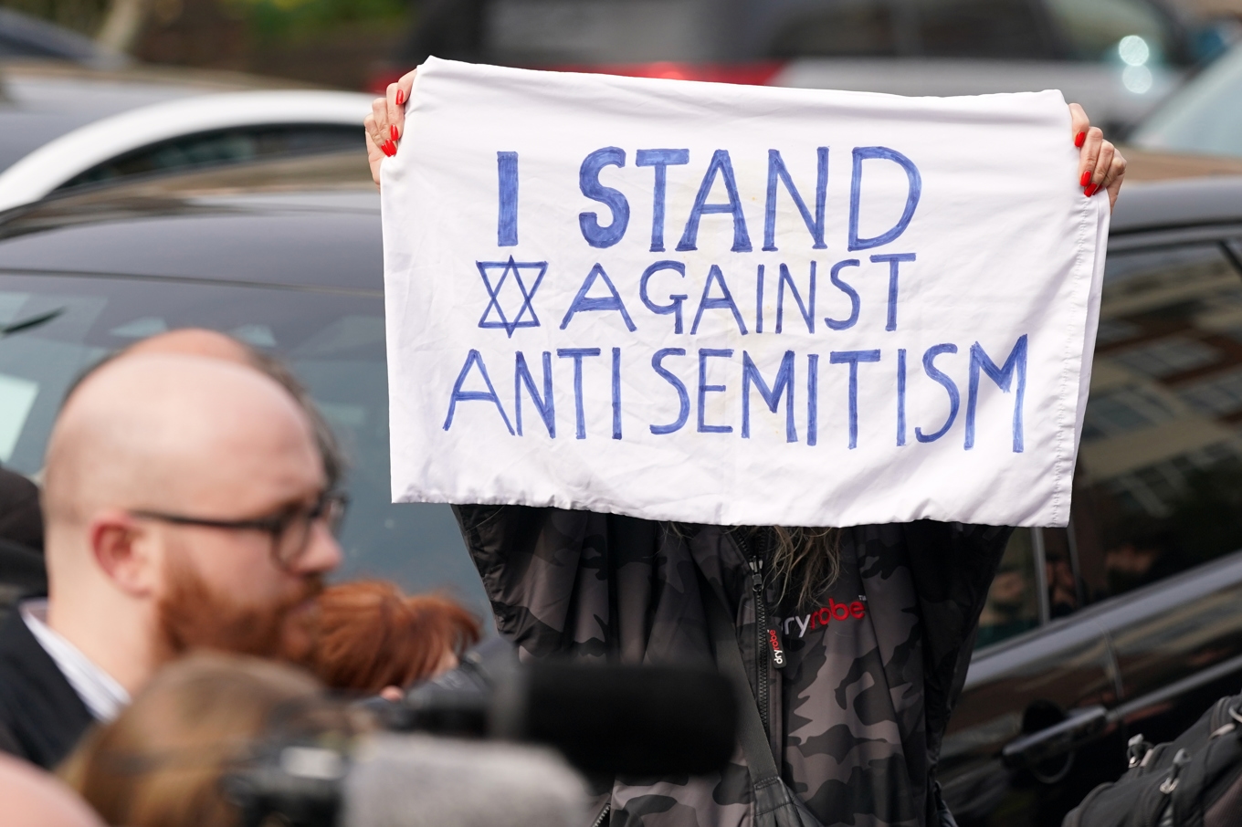 En demonstrant håller upp en banderoll efter en misstänkt mordbrand i mars 2026 mot fyra fordon som tillhörde den judiska ambulansorganisationen Hatzola Northwest i London. Foto: Alberto Pezzali/AP/TT