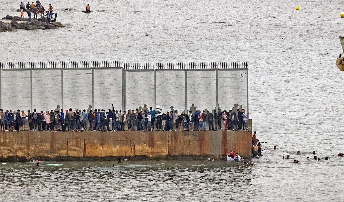 På bilden som är tagen den 18 maj 2021 ser man marockanska migranter samlas vid ett gränsstängsel i den norra staden Fnideq i ett försök att ta sig över gränsen från Marocko till Spaniens nordafrikanska exklaven Ceuta. Foto: Fadel Senna/AFP via Getty Images