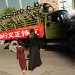 En muslimsk uigurkvinna med sin dotter försöker korsa en gata medan kinesisk militär kör förbi den stängda Grand Bazaar i uigurernas område i Urumqi den 9 juli. Några affärer har börjat öppna försiktigt, men den stora basaren i uigurernas område är fortfarande stängd, och uigurer säger att det är ännu ett exempel på de olika regler som gäller för uigurer jämfört med hankineser.