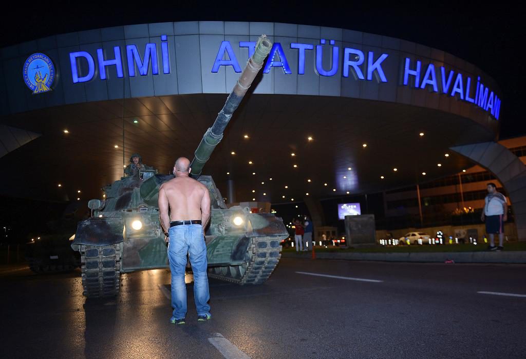 En man står, tidigt på lördagsmorgonen, framför en stridsvagn vid entrén till Atatürk-flygplatsen i Istanbul. (Foto: Ismail Coskun/IHA/AP/TT)